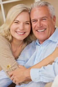 Older couple smiling together at home, showing their teeth